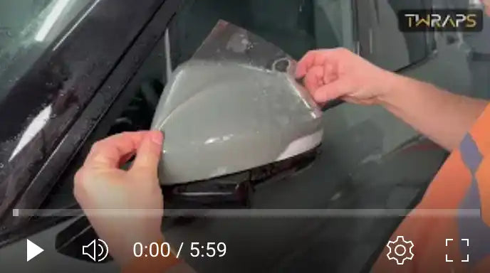 Hands peeling a protective film or covering from what appears to be a car side mirror.