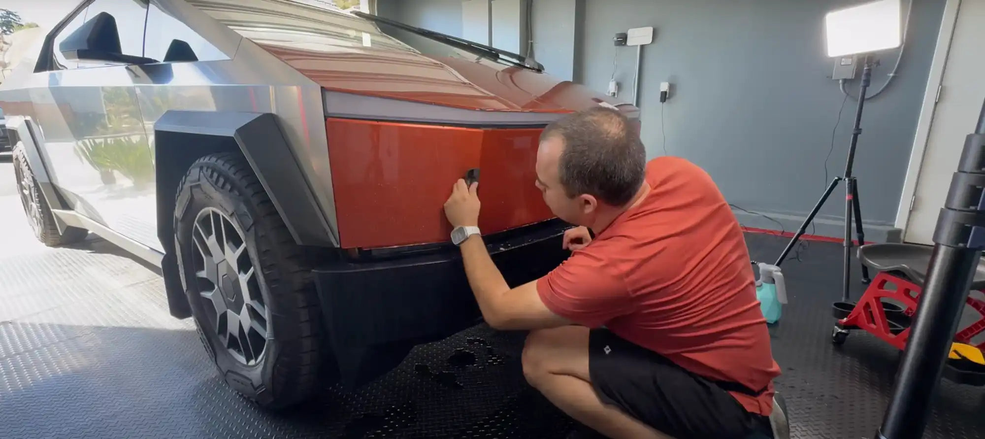 Person in a red shirt applying a coating or treatment to a vehicle’s wheel well or fender.