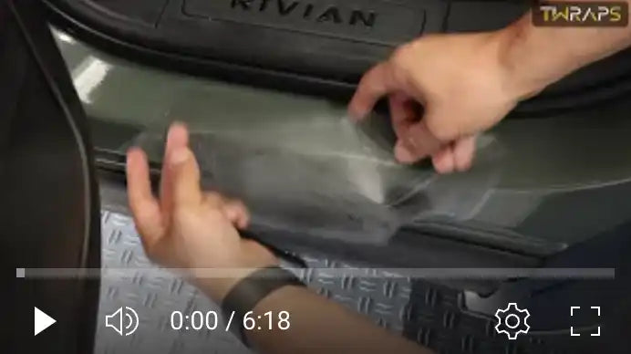 Video player showing hands applying what appears to be a protective film or wrap to a Rivian vehicle.