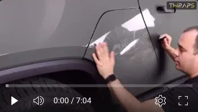 Video player showing someone applying what appears to be a protective film or wrap to a vehicle.